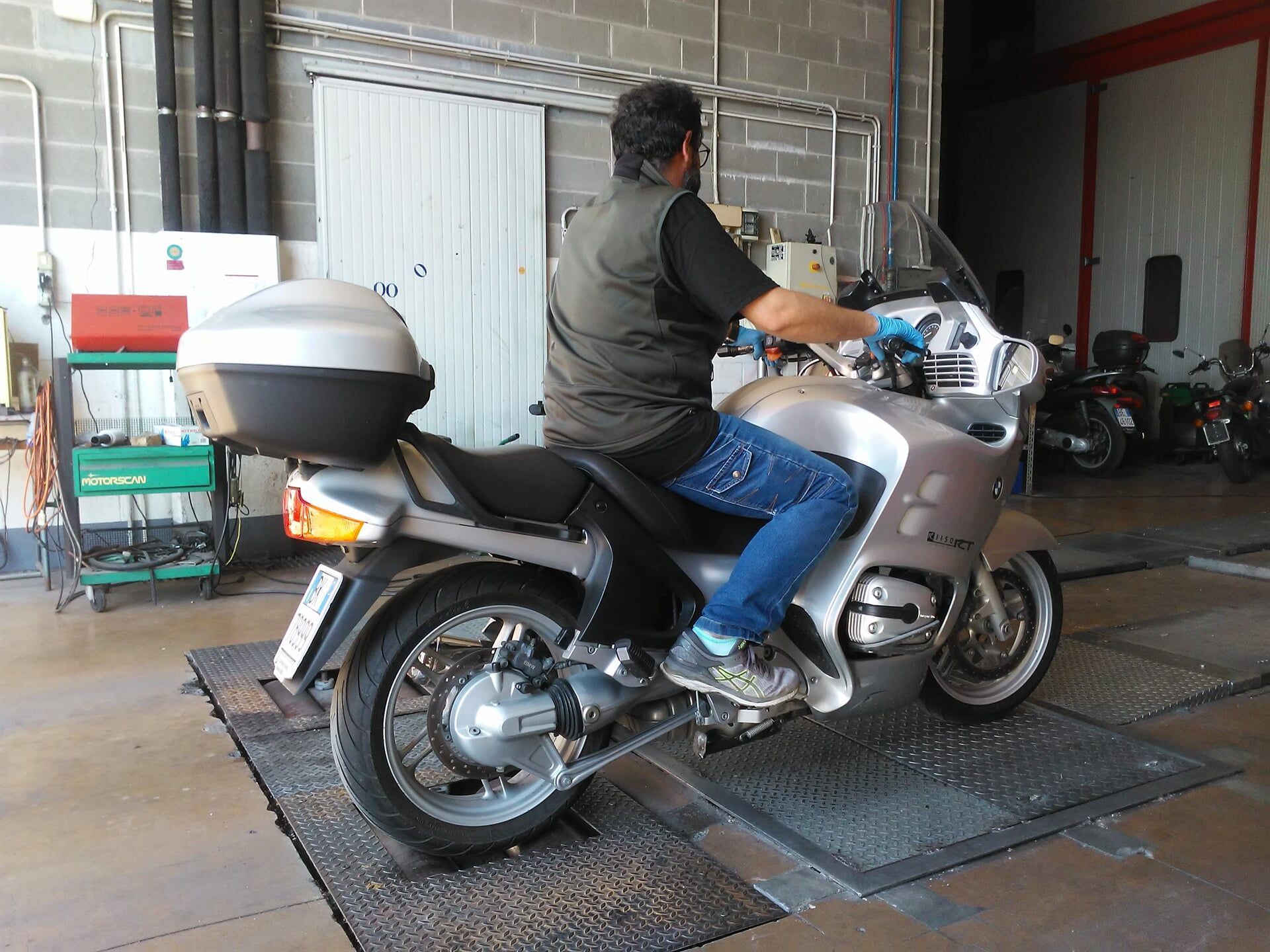 Uomo su una motocicletta argentata all'interno di un garage per l'ispezione.