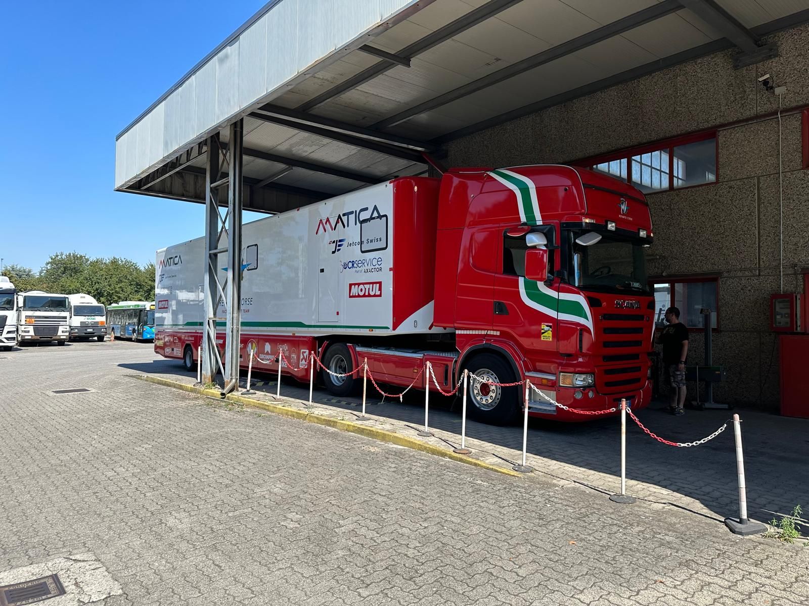Un camion MATICA rosso e bianco parcheggiato sotto un'area coperta, accanto a un edificio.