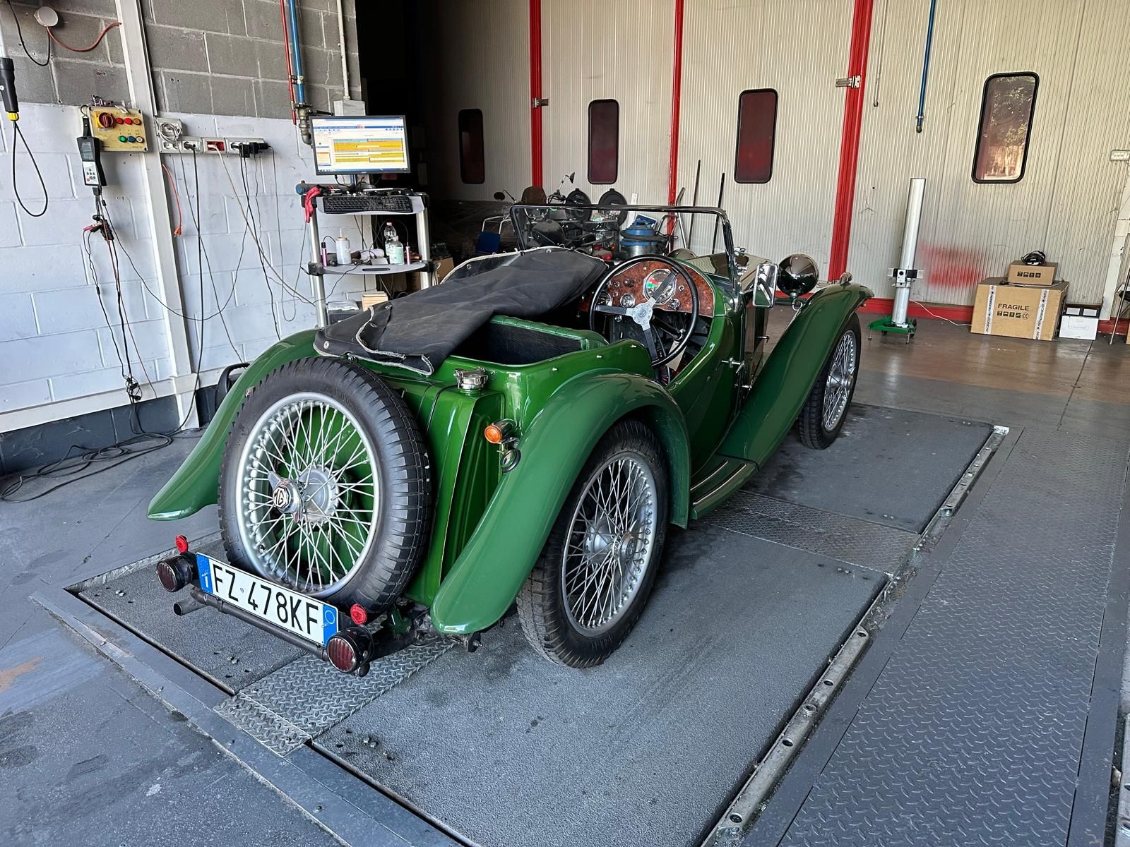 Un'auto d'epoca decappottabile verde su un dinamometro in un garage, sottoposta a test.
