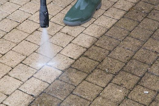 worker power washing concrete surface of home