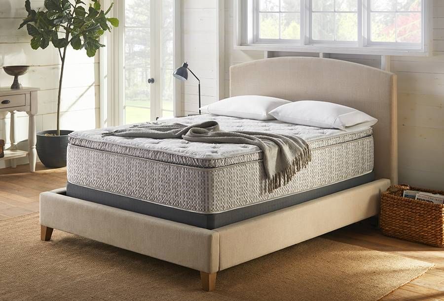 White bedding on the floor near a white paneled door, beige curtain to the left, on a wooden floor.