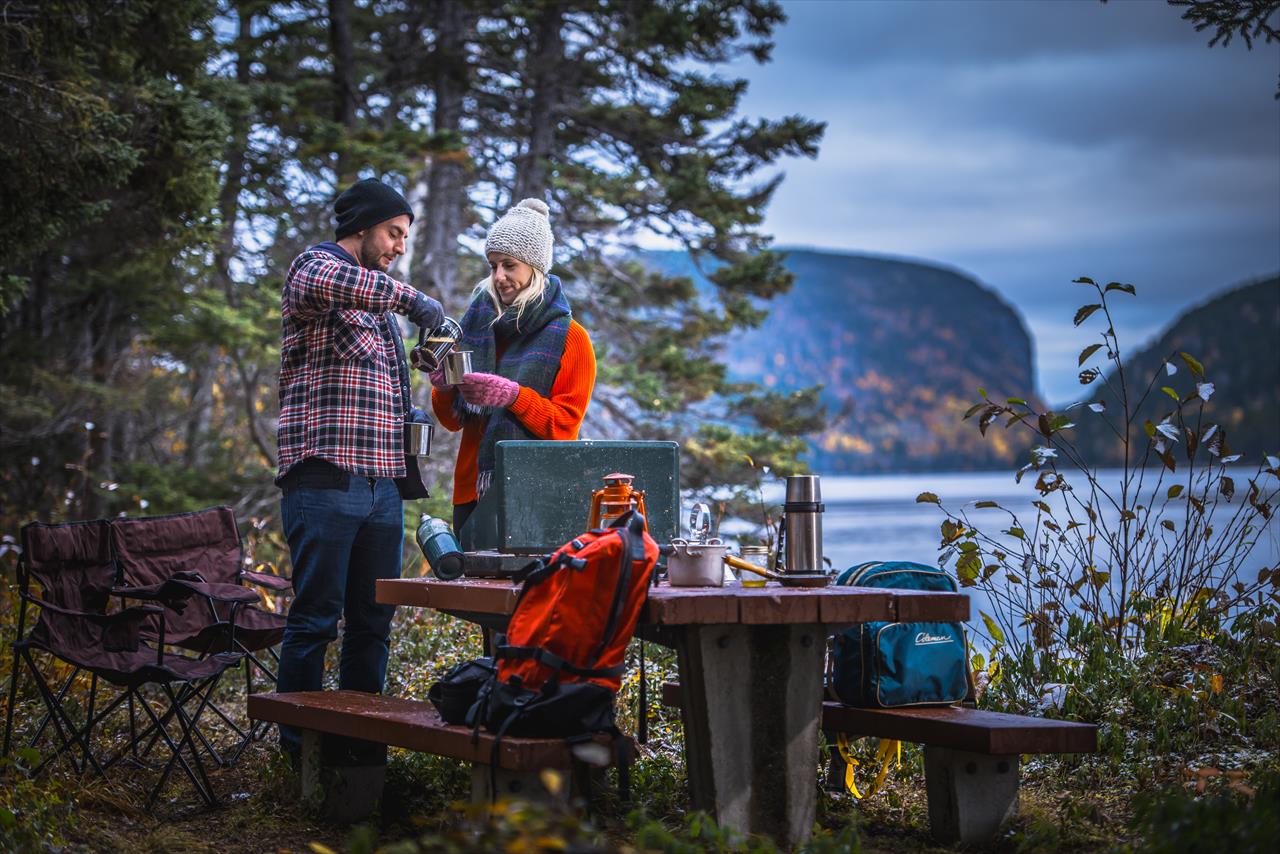Deux personnes partagent un café au bord de l'eau. On peut voir les collines de Terra-Nova derrière