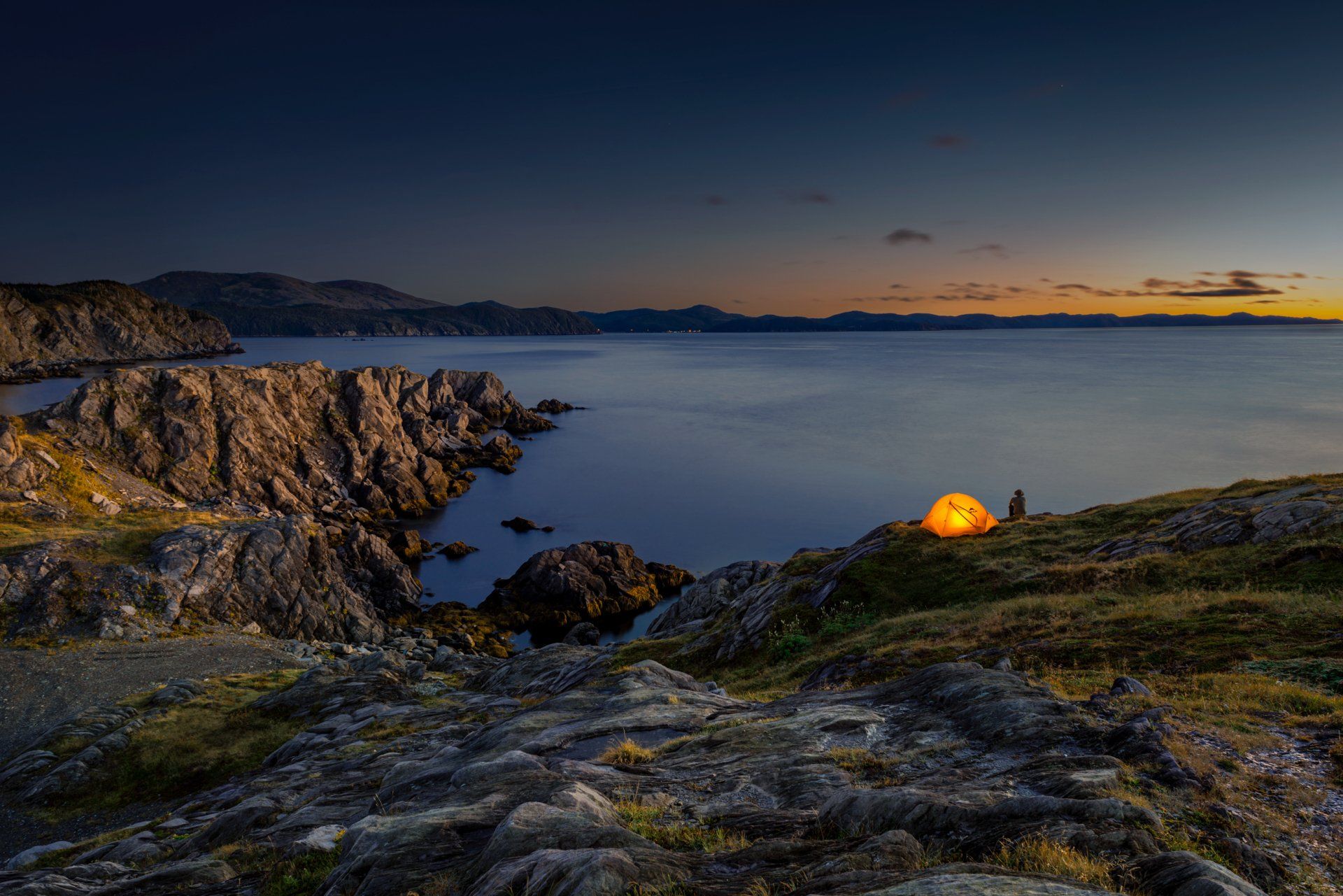 Un campeur assis près de sa tente regarde la nuit tomber sur la côte dans l'est de Terre-Neuve