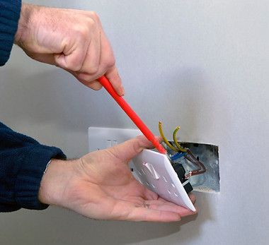 A person is fixing a light switch with a red screwdriver