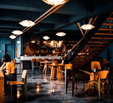 A woman is sitting at a table in a restaurant with tables and chairs.