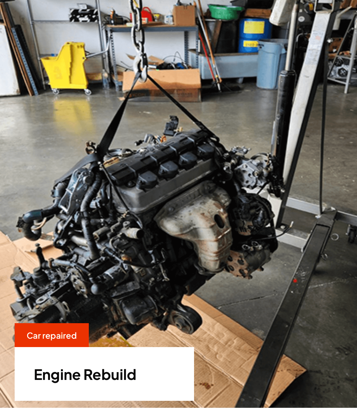 Engine being rebuilt, hanging from a crane in a garage.