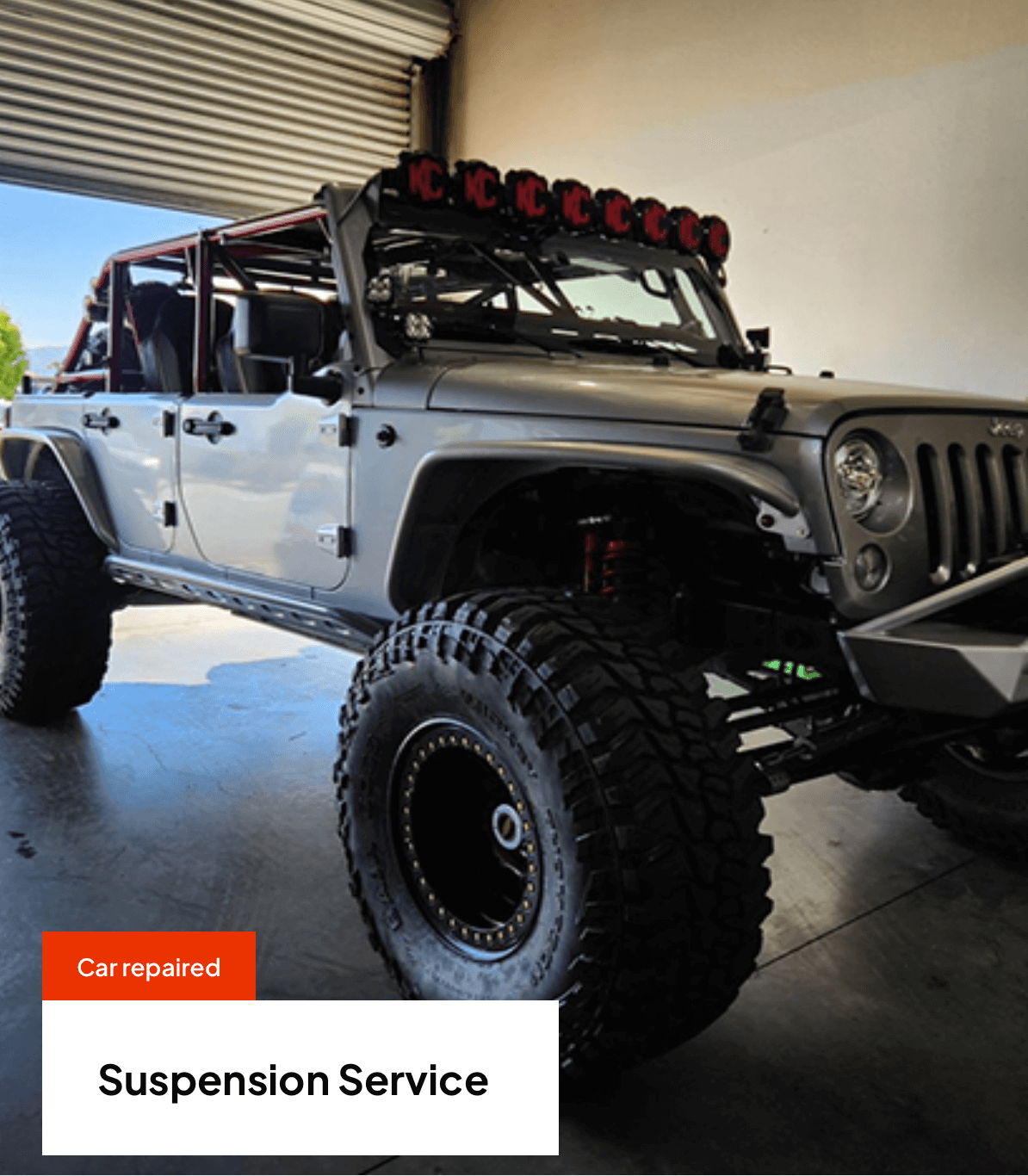 Grey lifted Jeep with oversized tires, roll cage, and LED lights.