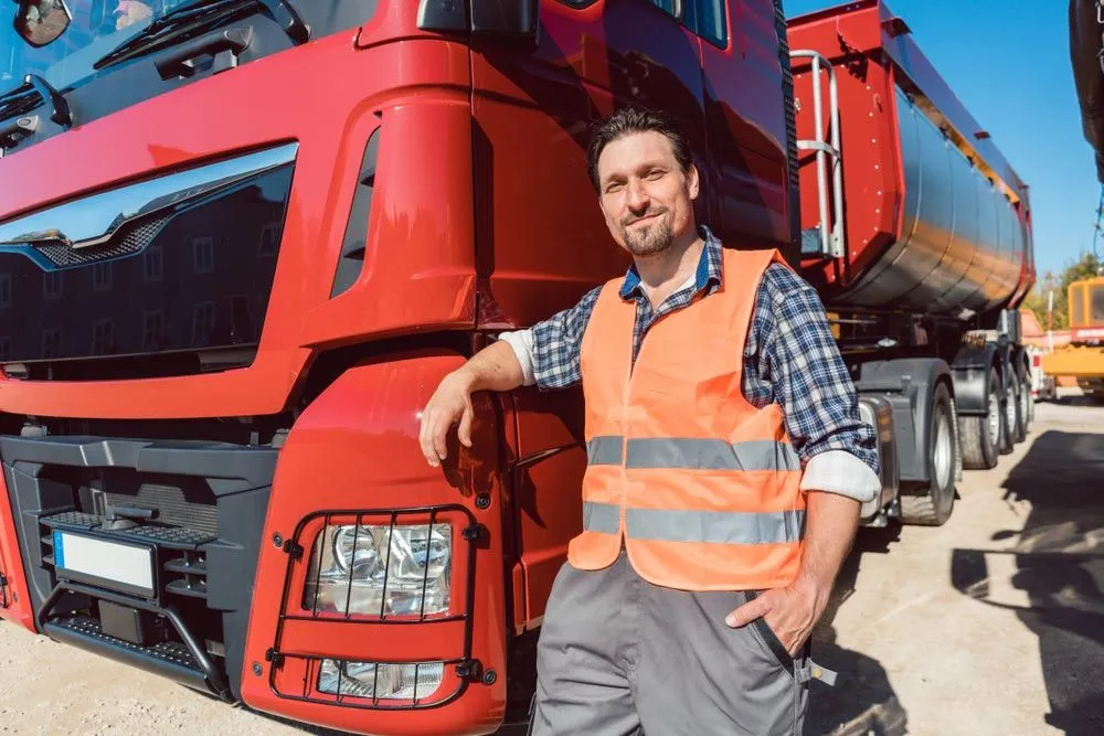 A Man is Leaning Against the Side of a Red Semi Truck — Truck Training and Assessments In Umina Beach, NSW