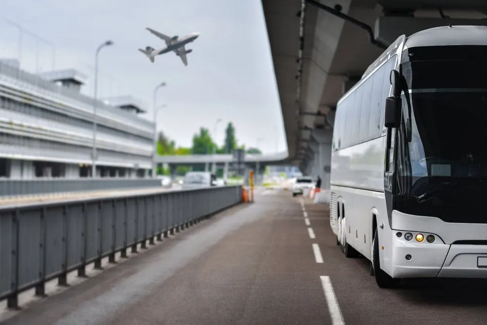 A White Bus is Driving Down a Highway Next to an Airport — Truck Training and Assessments In Umina Beach, NSW