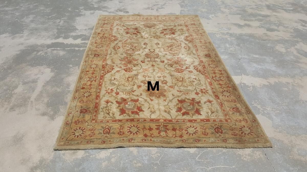 A rug with the letter m on it is sitting on a concrete floor.