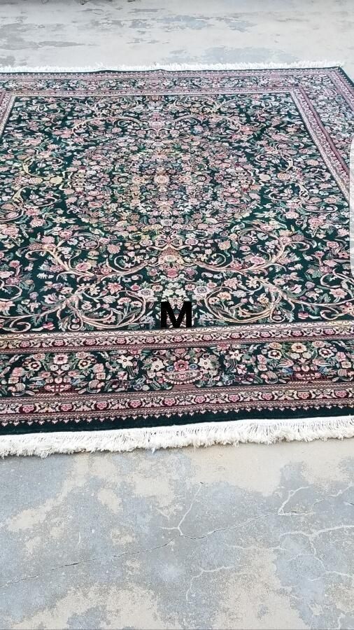 A rug with the letter m on it is sitting on a concrete floor.