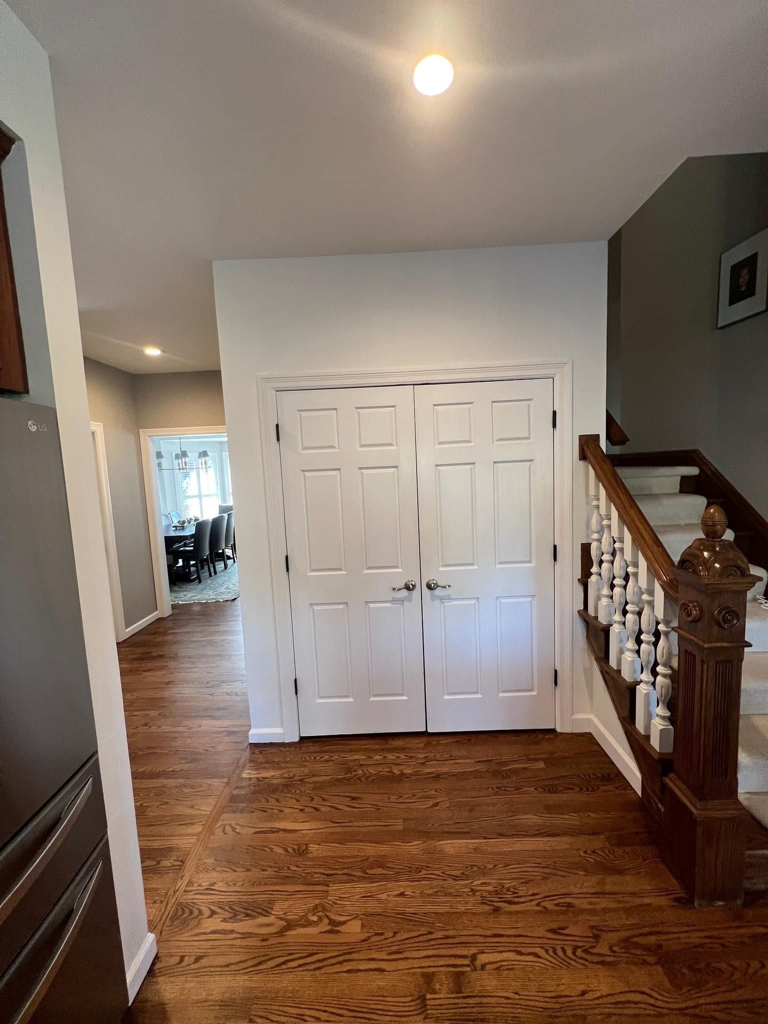 A hallway with hardwood floors and white doors leading to a staircase.