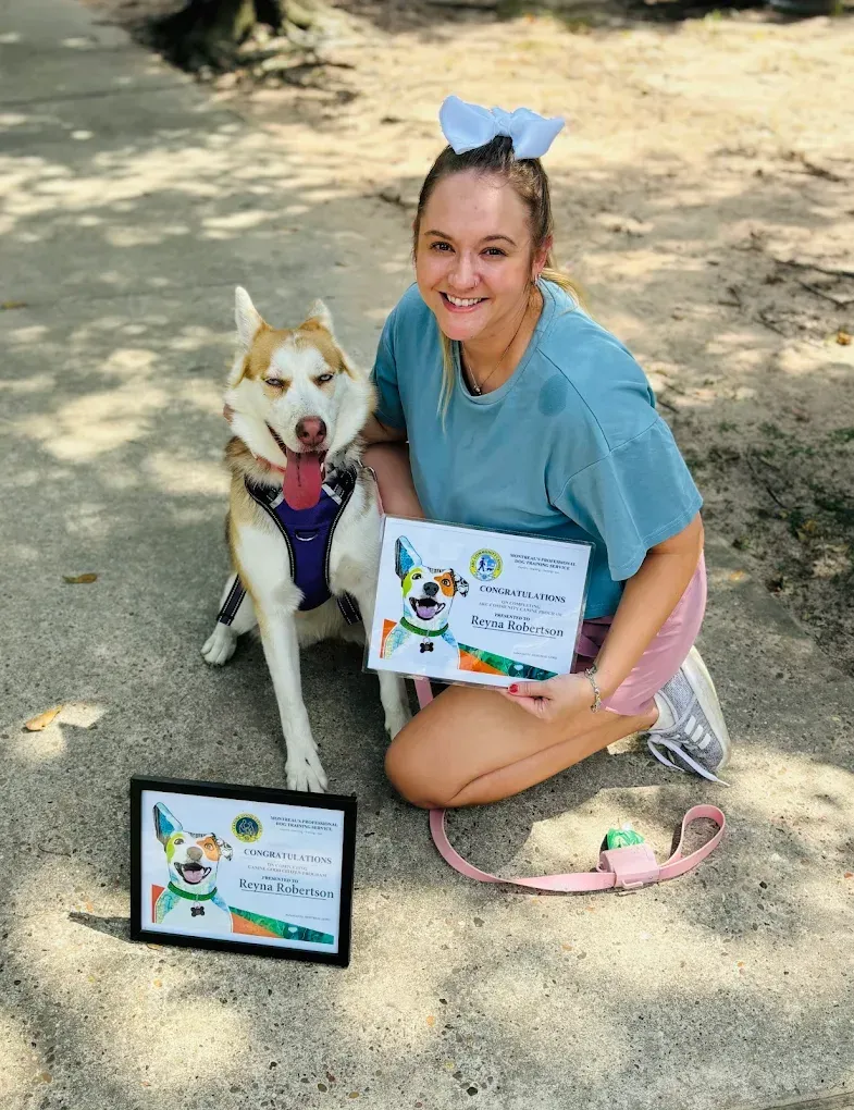 Woman kneels with a husky, holding certificates, at a park. Both smile.