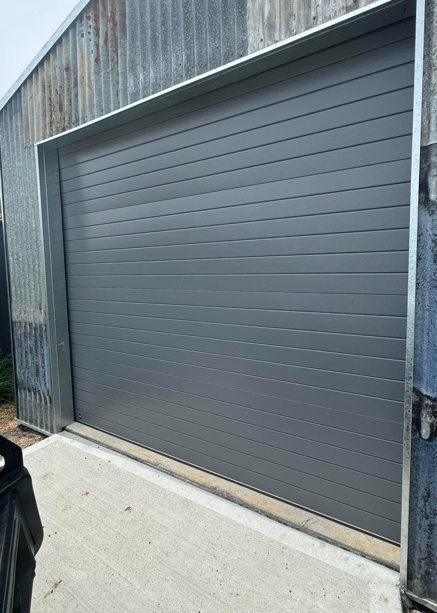 A gray garage door is sitting on the side of a building.
