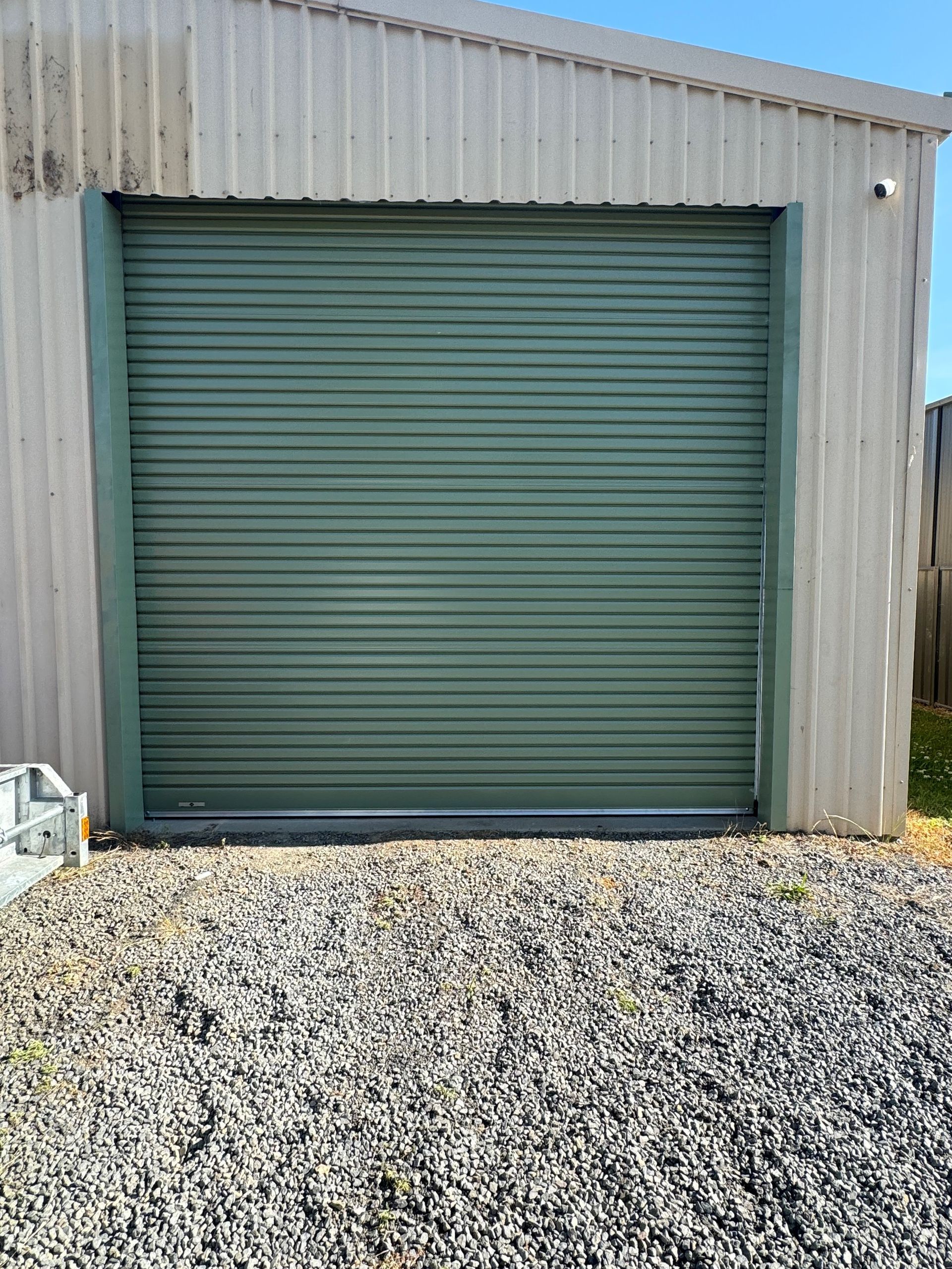 A green garage door is sitting on top of a gravel driveway.