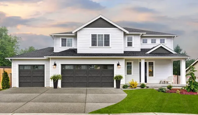 Two-car garage with beige doors, a gray roof, and a driveway leading up to it.