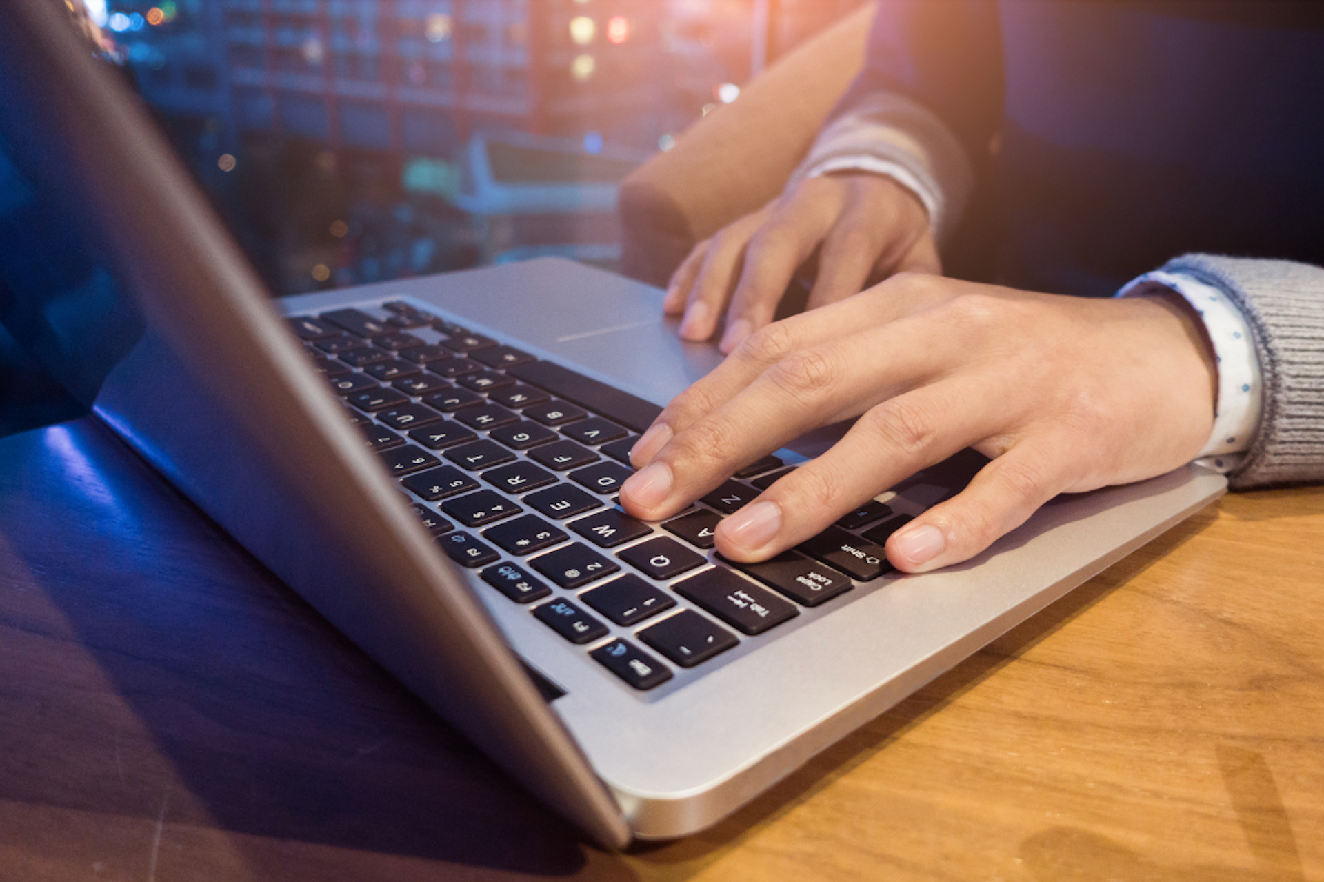 A person is typing on a laptop computer on a wooden table.