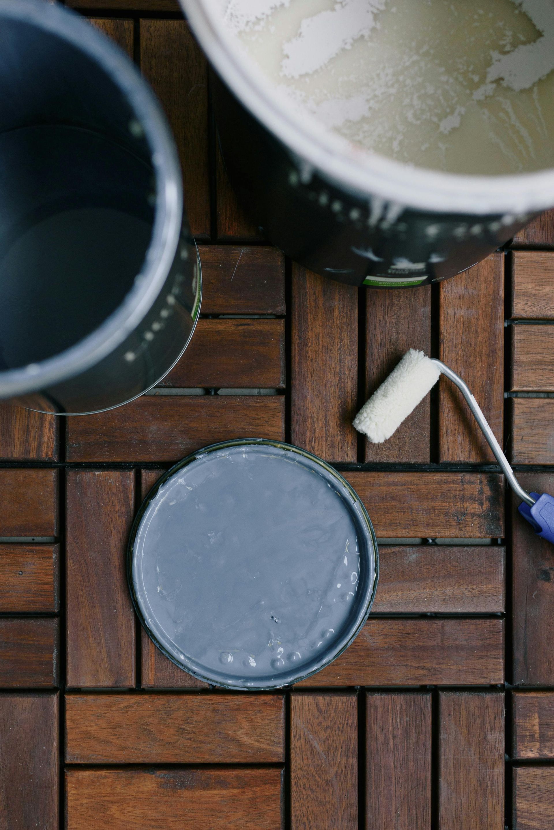 A bucket of paint and brush on a wooden floor