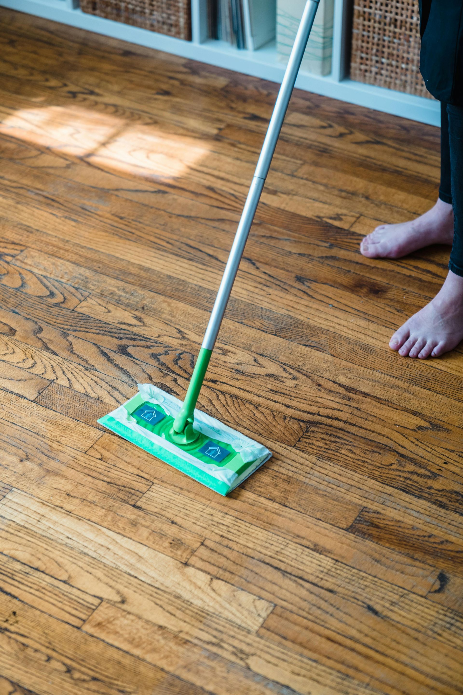 A person cleaning hardwood floors with a mop, showcasing a polished wooden surface and a tidy living space in the background.