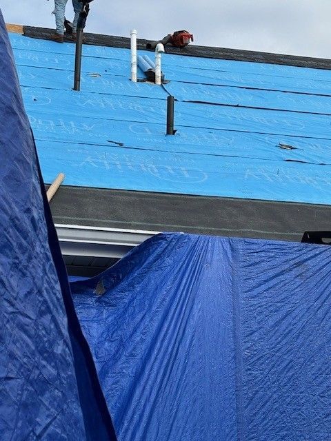 Blue tarp on roof under construction with affordable roofing services roofer standing on top