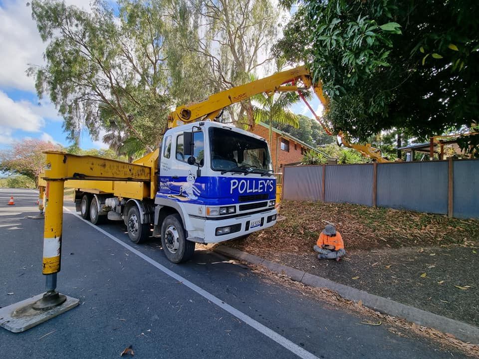 A Yellow Truck With a Crane on the Back is Parked on the Side of the Road — Polley's Concrete Pumping in Kuttabul, QLD