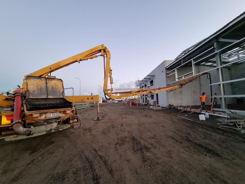 A Yellow Truck With a Crane is in Front of a Building Under Construction — Polley's Concrete Pumping in Kuttabul, QLD