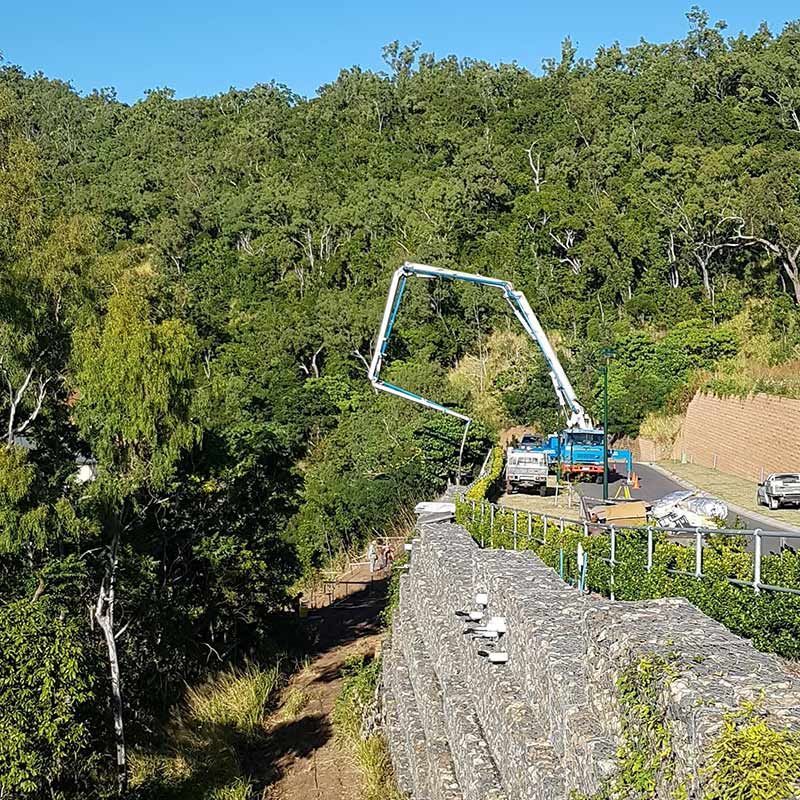 A Truck is Driving Down a Road Next to a Stone Wall — Polley's Concrete Pumping in Sarina, QLD