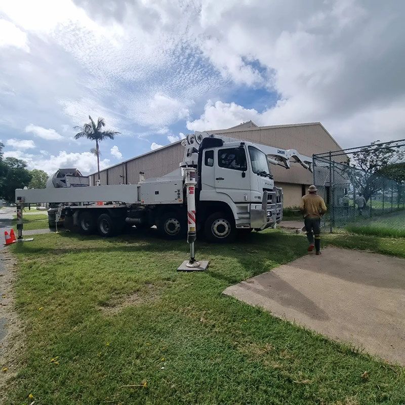 A White Truck With a Crane on the Back is Parked in a Grassy Area — Polley's Concrete Pumping in Kuttabul, QLD