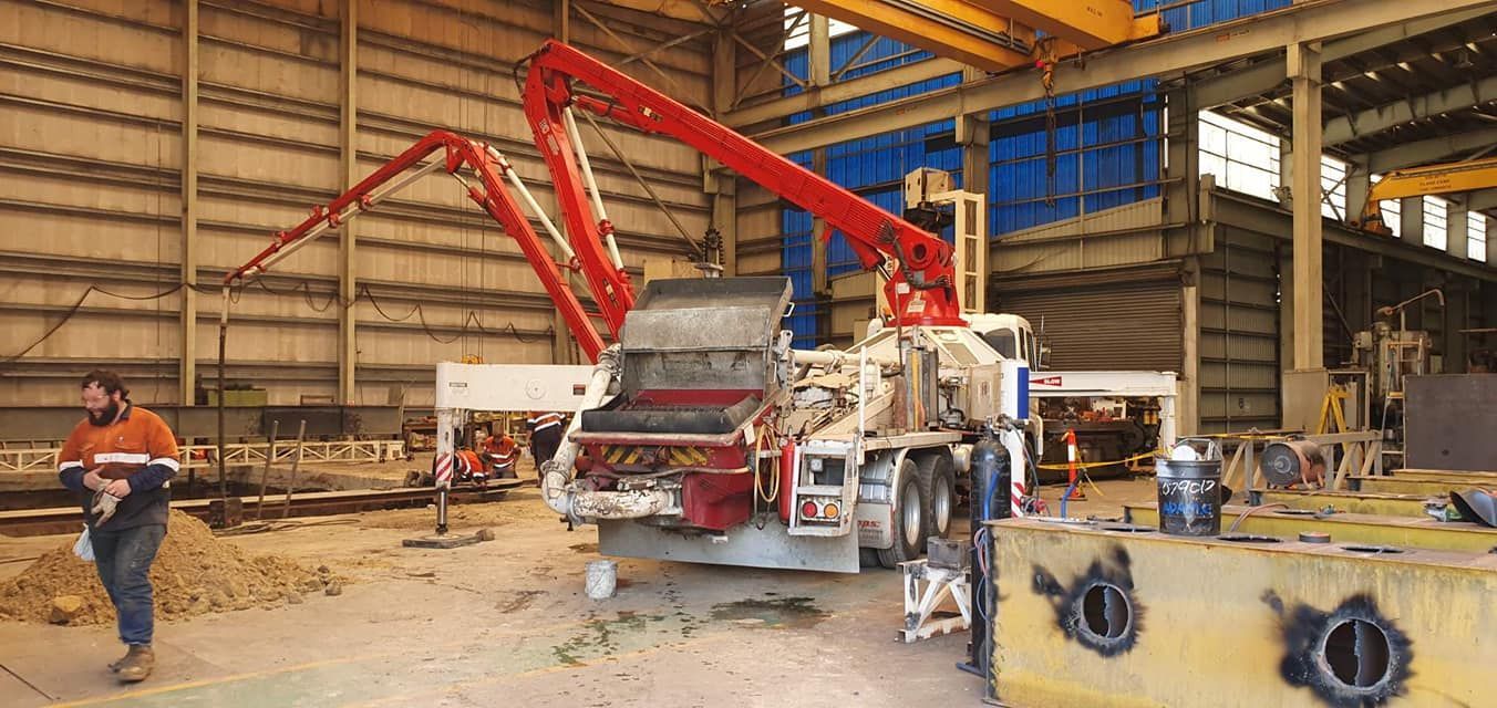 A Man is Standing Next to a Concrete Pump in a Large Building — Polley's Concrete Pumping in Marian, QLD