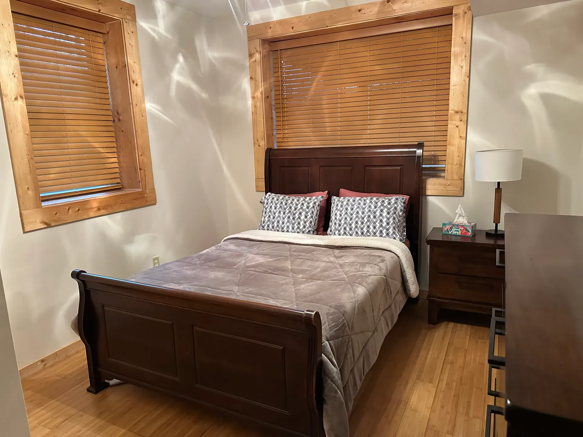 A bedroom with a bed , nightstand , lamp and two windows