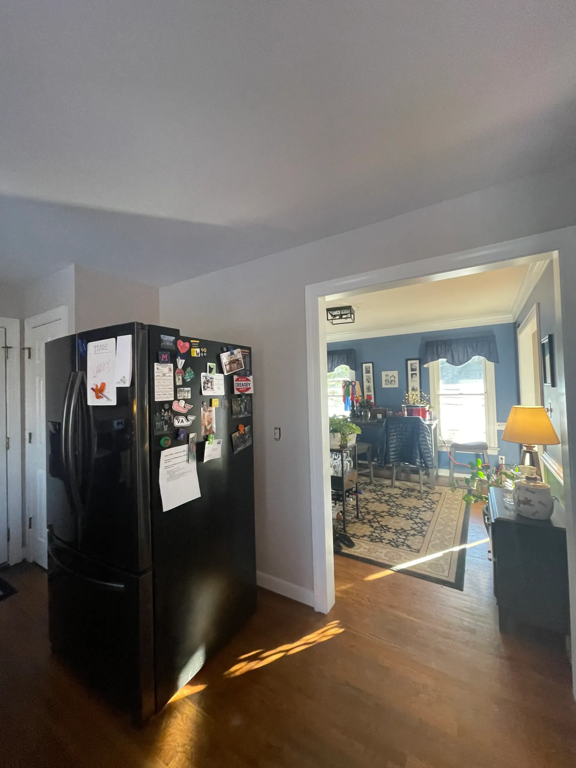 A black refrigerator is sitting in a living room next to a dining room.