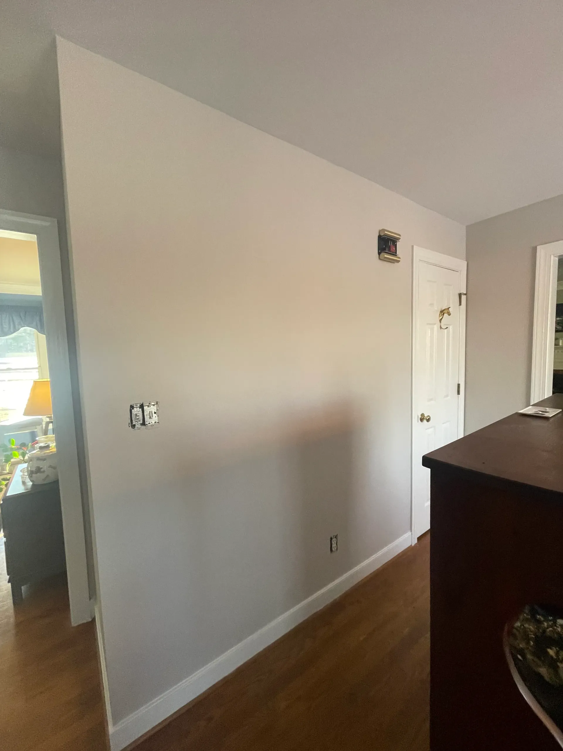 A hallway in a house with a white wall and a wooden floor.