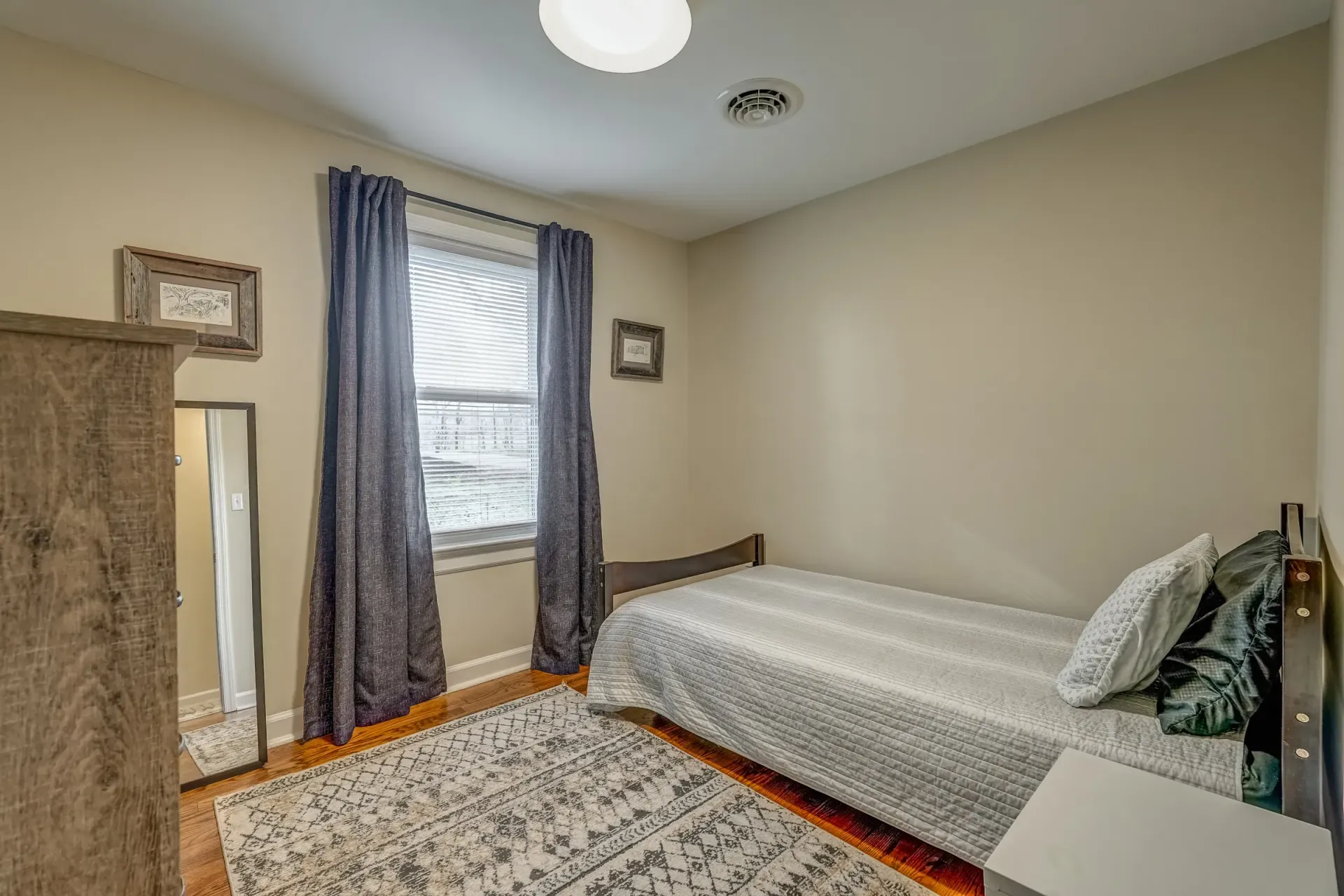 A bedroom with a single bed , a rug , a mirror and a window.