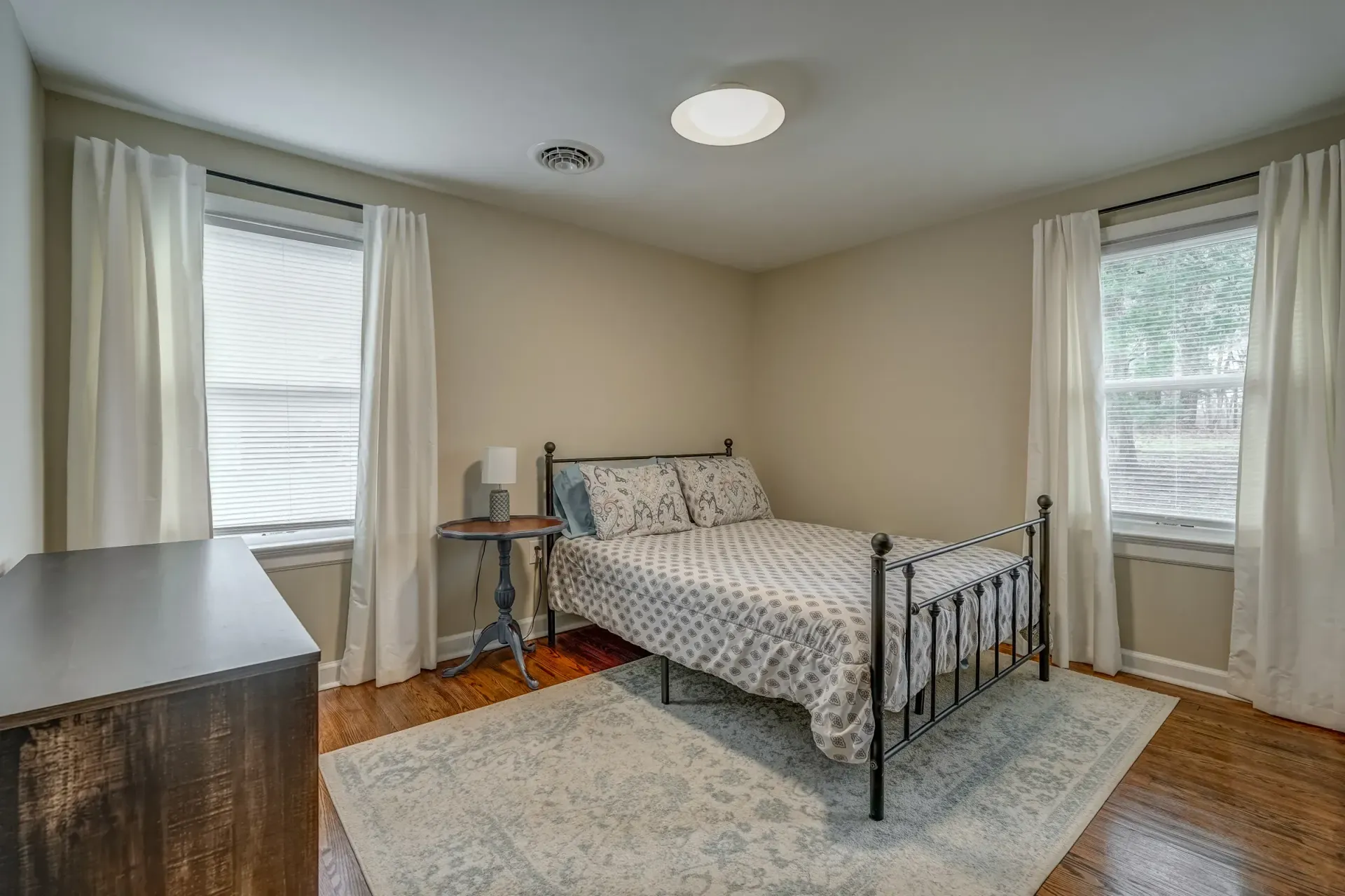 A bedroom with a bed , dresser , and two windows.