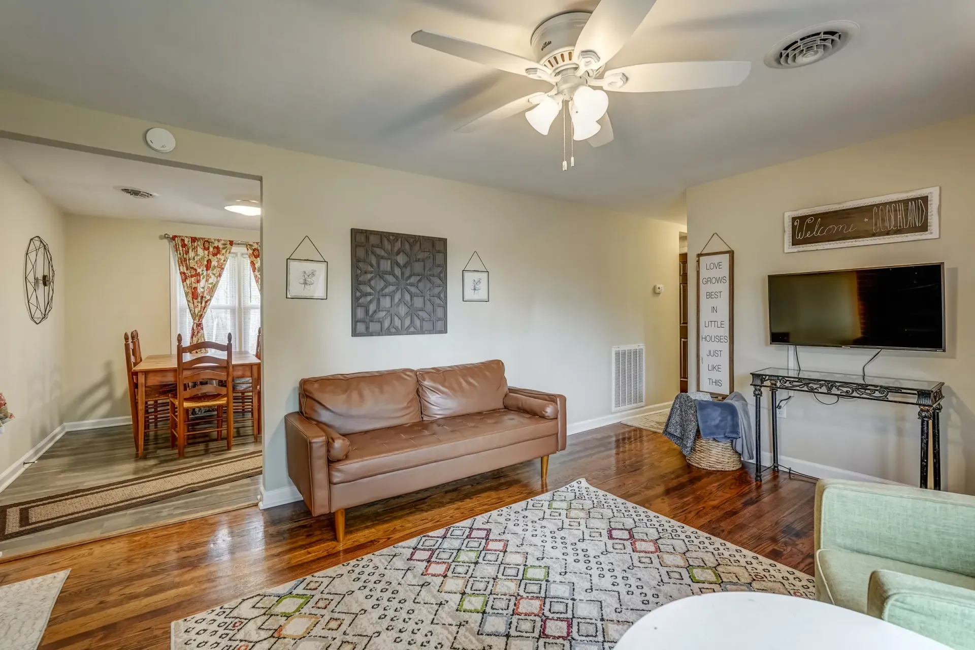 A living room with a couch , chair , television and ceiling fan.