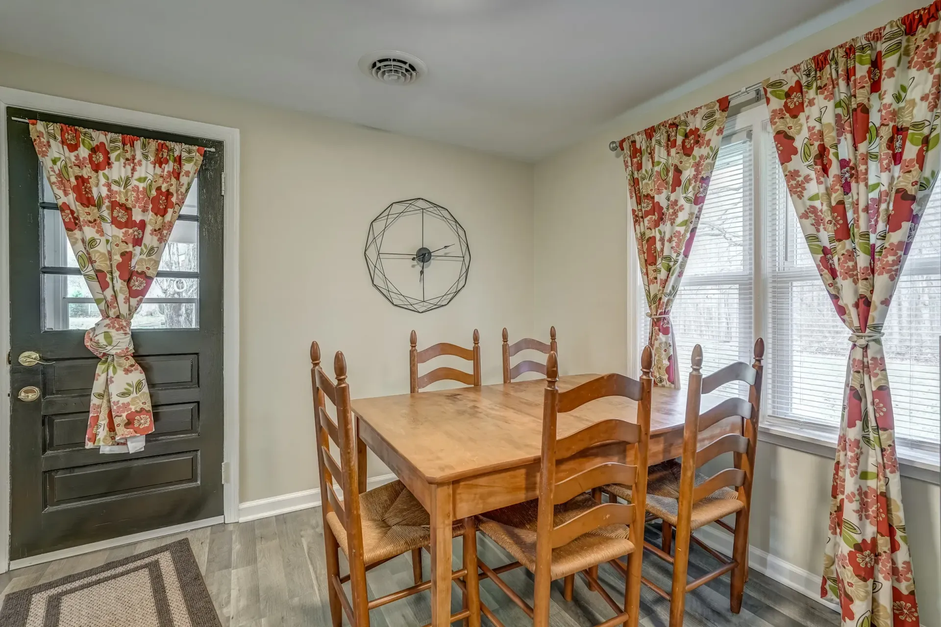 A dining room with a table and chairs and a clock on the wall.