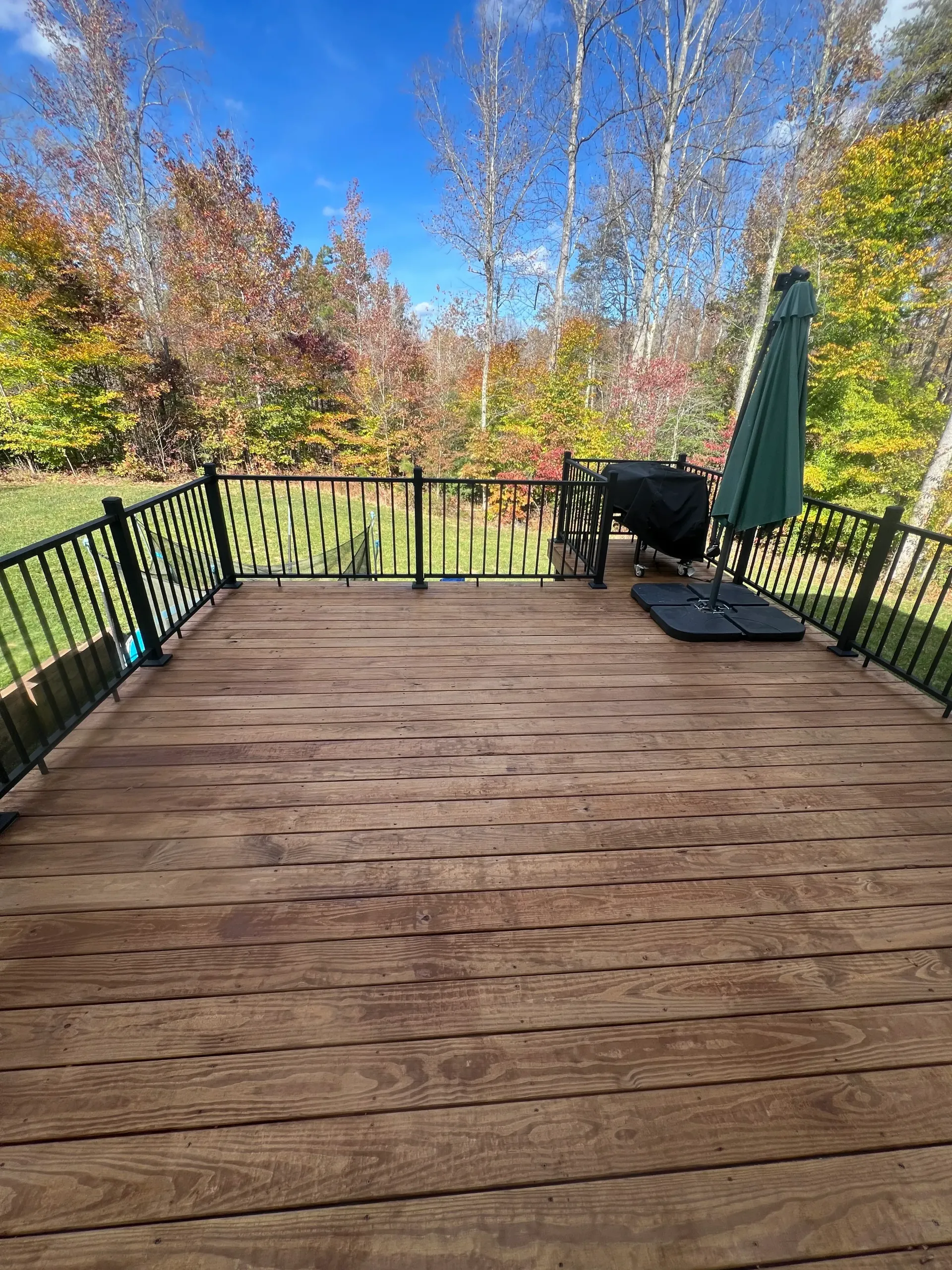 A wooden deck with a green umbrella and a grill.