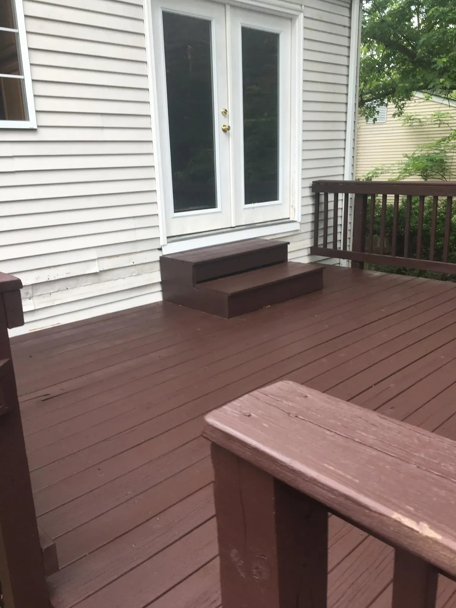 A wooden deck with stairs and a white house in the background.