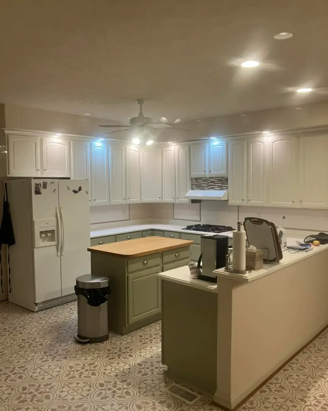 A kitchen with white cabinets , a refrigerator , a stove , a sink , and a trash can.