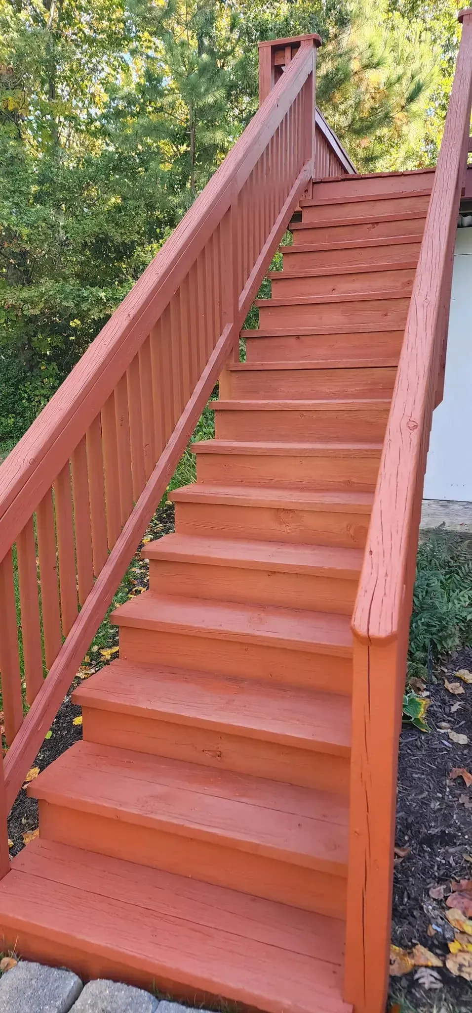 A wooden staircase with a red railing leading up to a house.