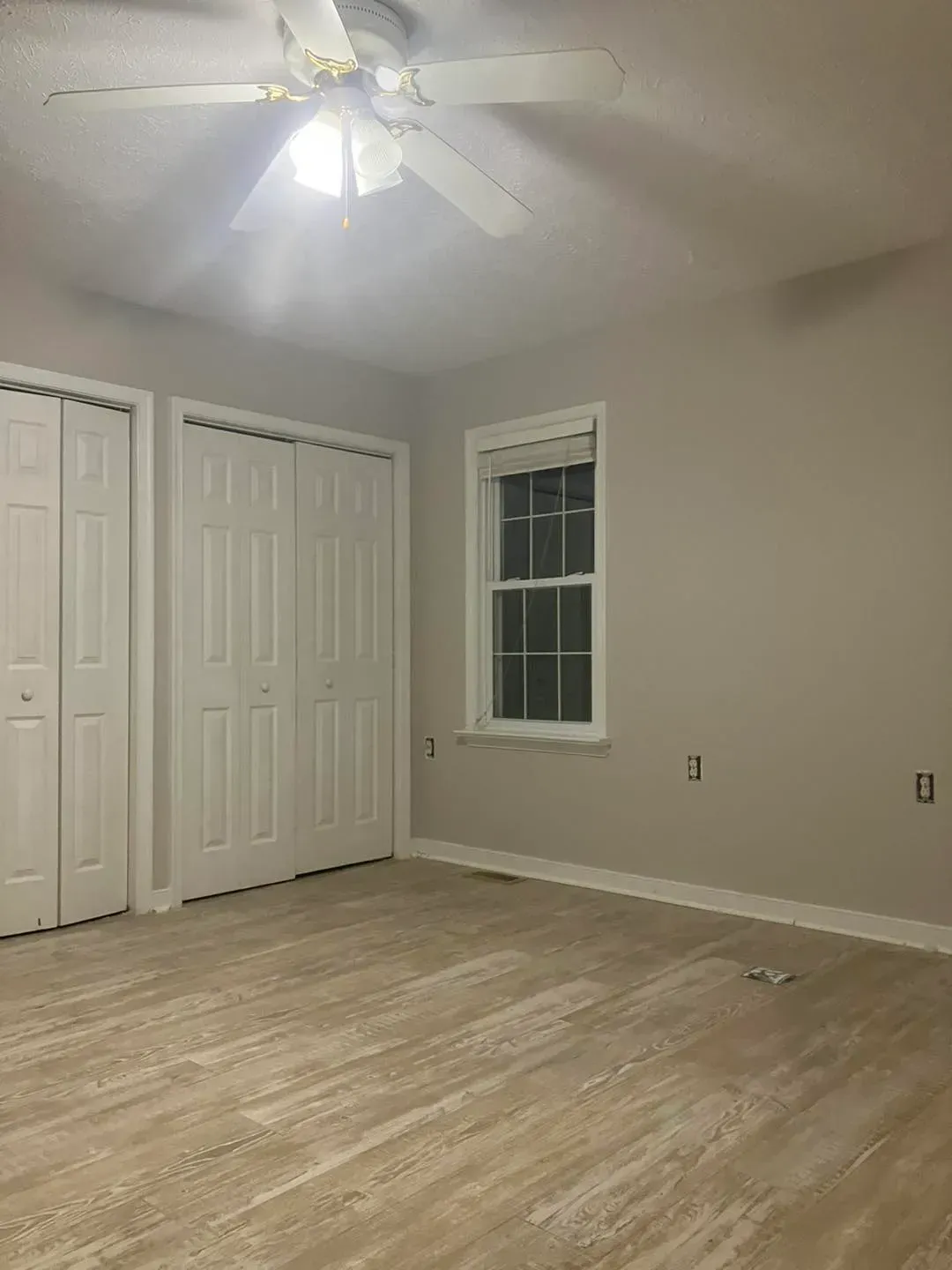 An empty bedroom with a ceiling fan and a window.
