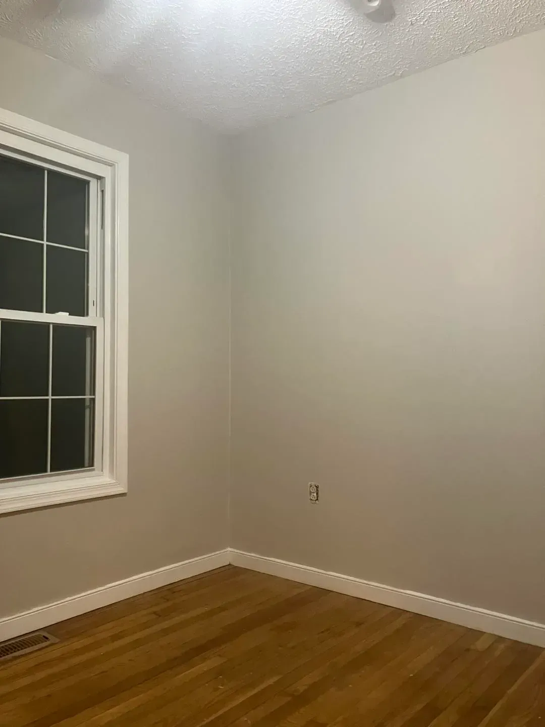 An empty room with a window and hardwood floors.
