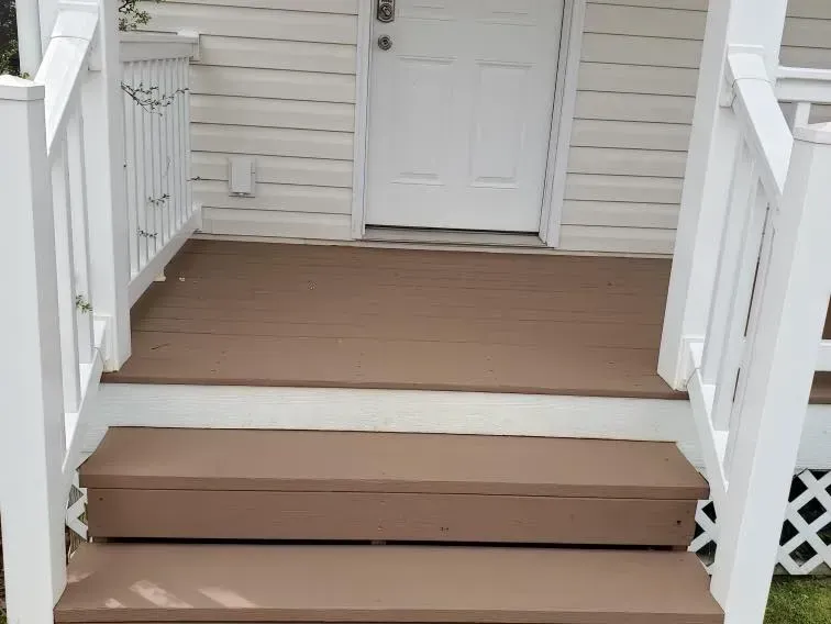 The front porch of a house with brown steps and a white railing.