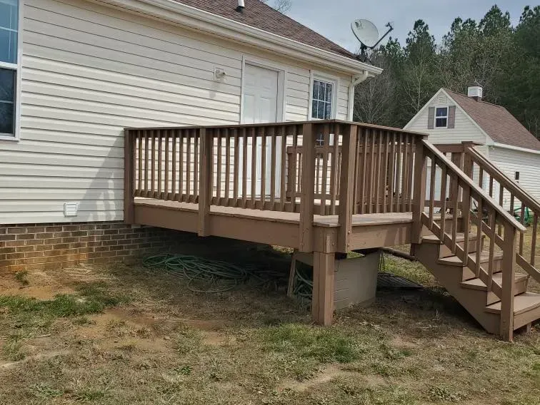 A wooden deck with stairs leading up to it is in front of a house.