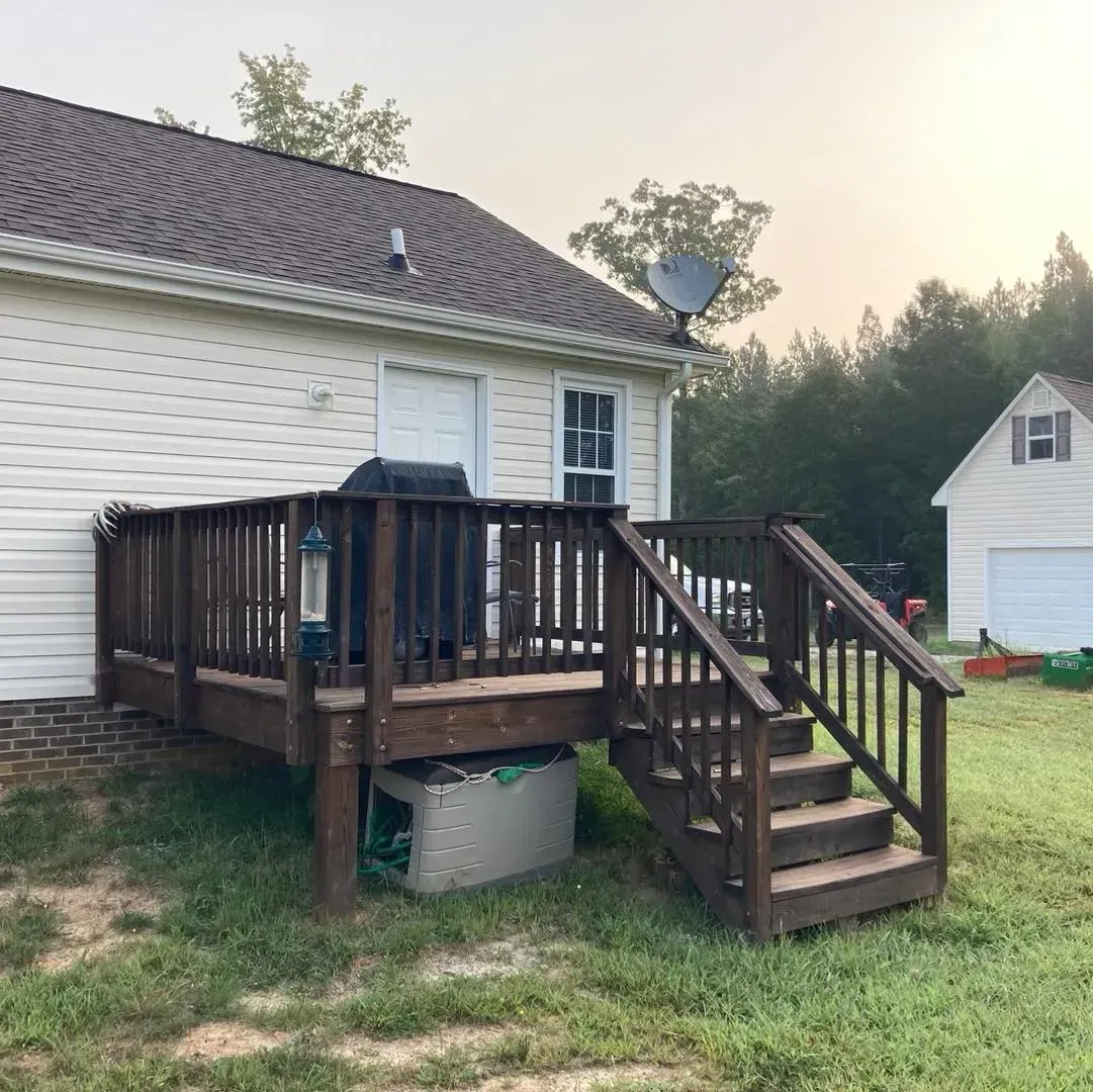 A white house with a wooden deck and stairs in front of it.