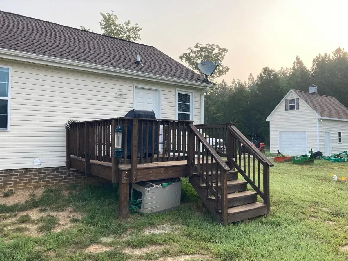 A white house with a wooden deck and stairs in front of it.