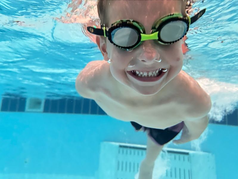 A young boy wearing goggles is swimming underwater in a pool.