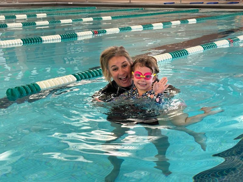 A woman is teaching a little girl how to swim in a swimming pool.