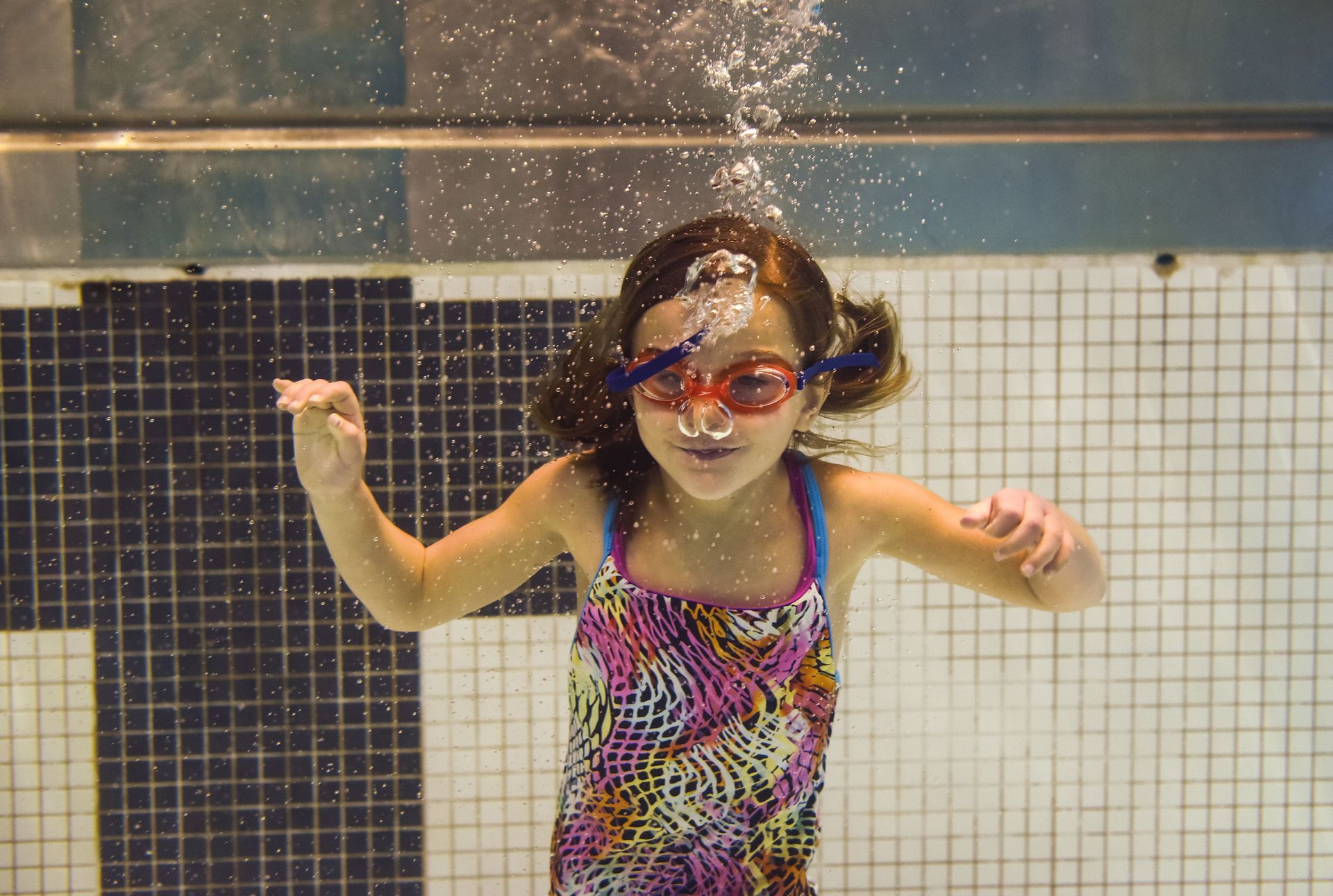 A little girl is swimming underwater in a swimming pool.