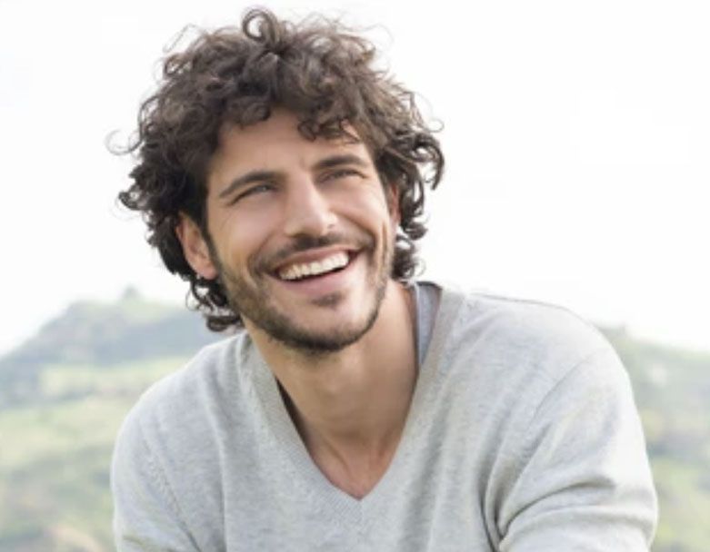 A man with curly hair and a beard is smiling.